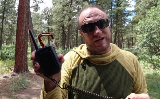 Man holding a walkie talkie with coiled cable in a forest, demonstrating long-range two-way radio use outdoors